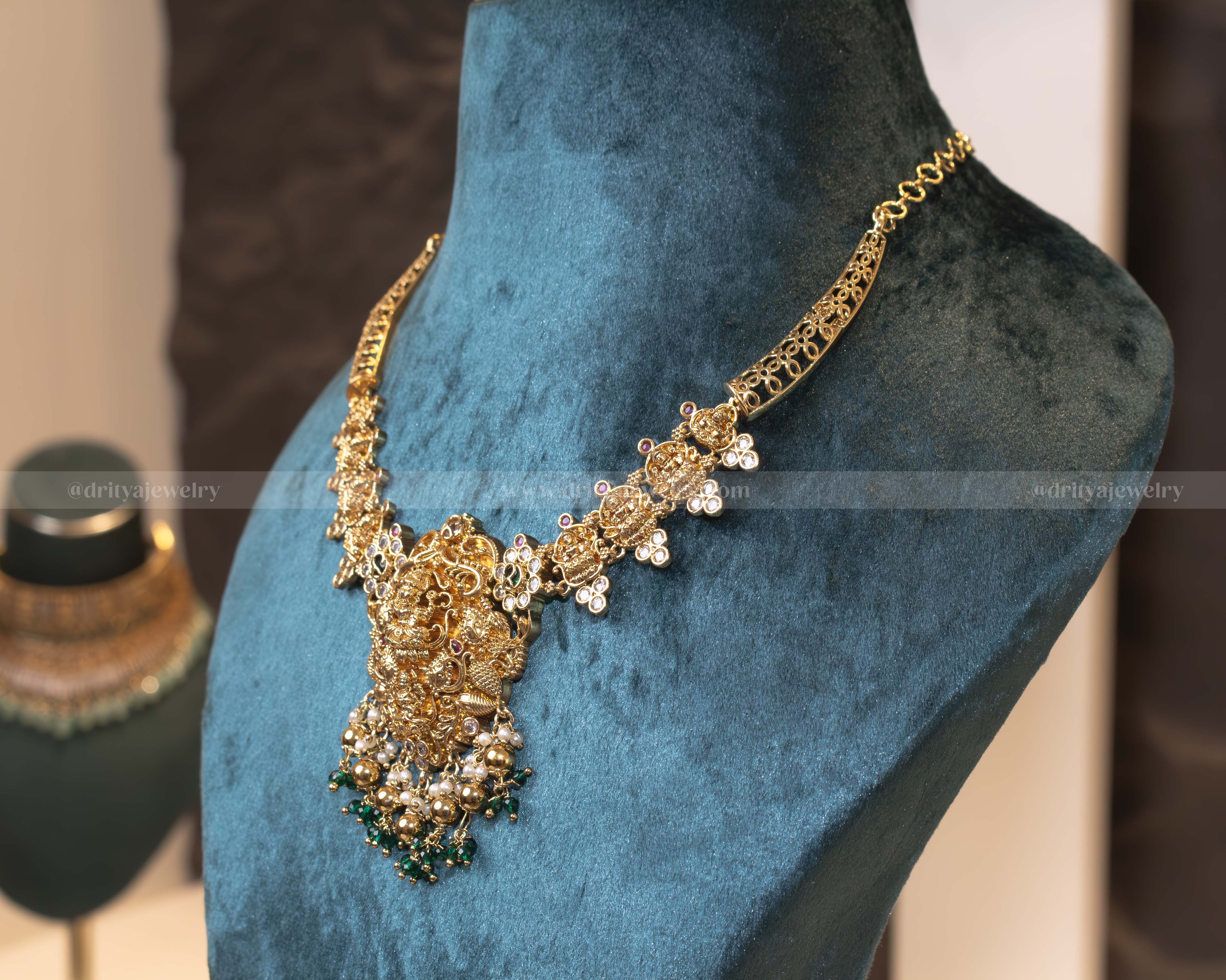 Temple kanti necklace set featuring intricate gold temple motifs, sparkling stones, pearls, green beads, and matching jhumka earrings.