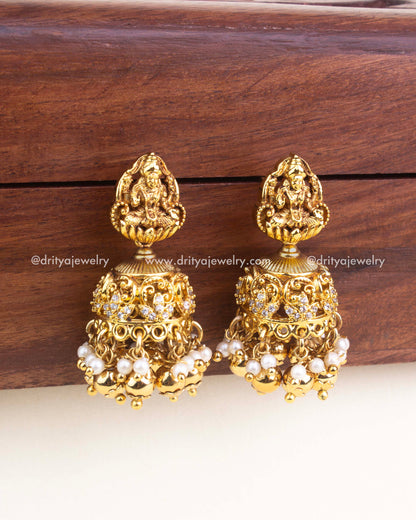 Pair of antique gold jhumka earrings featuring Lakshmi carving, AD accents, and pearl drops
