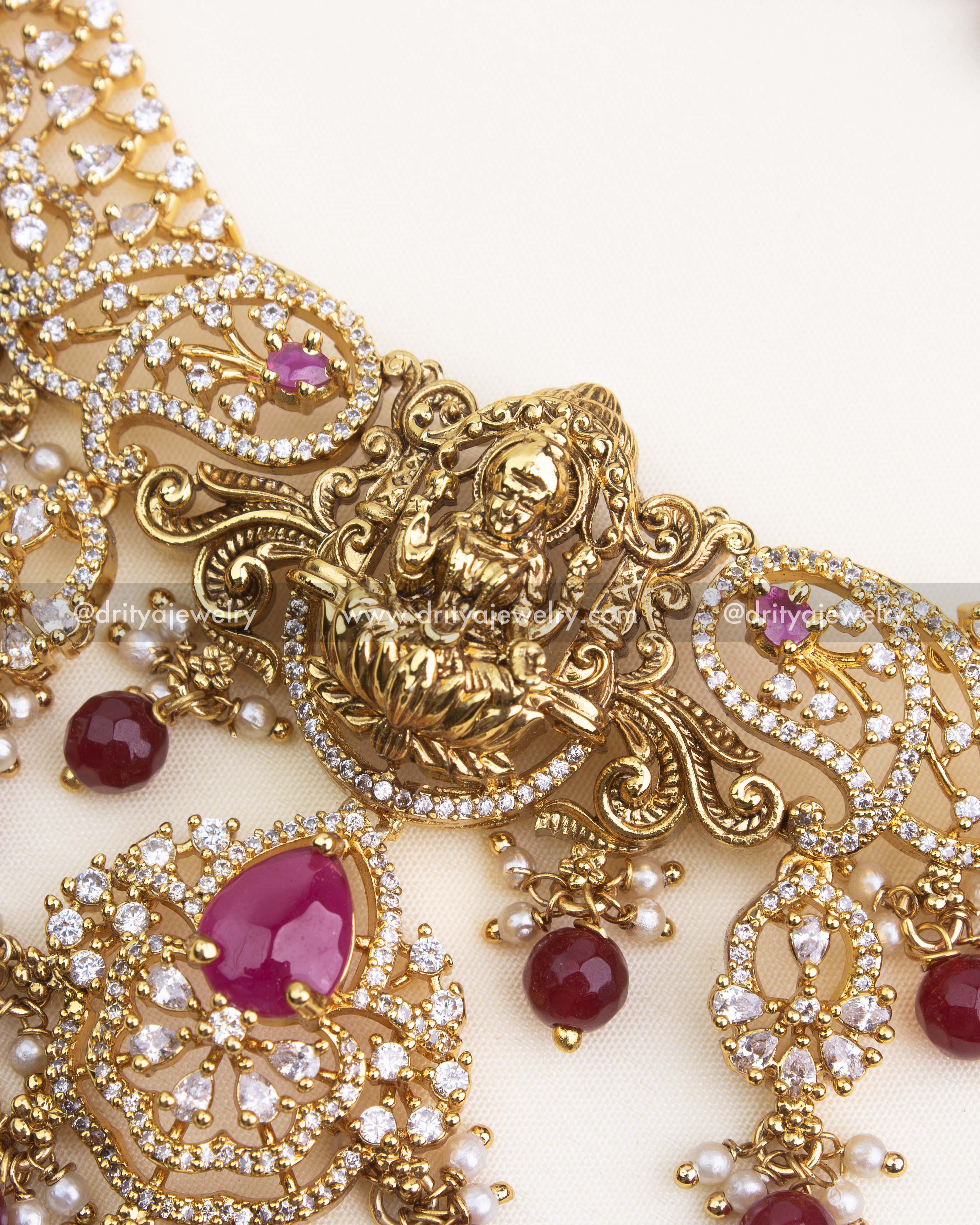 Close-up of ruby red teardrop stone and CZ detailing on temple-style necklace with Lakshmi pendant.