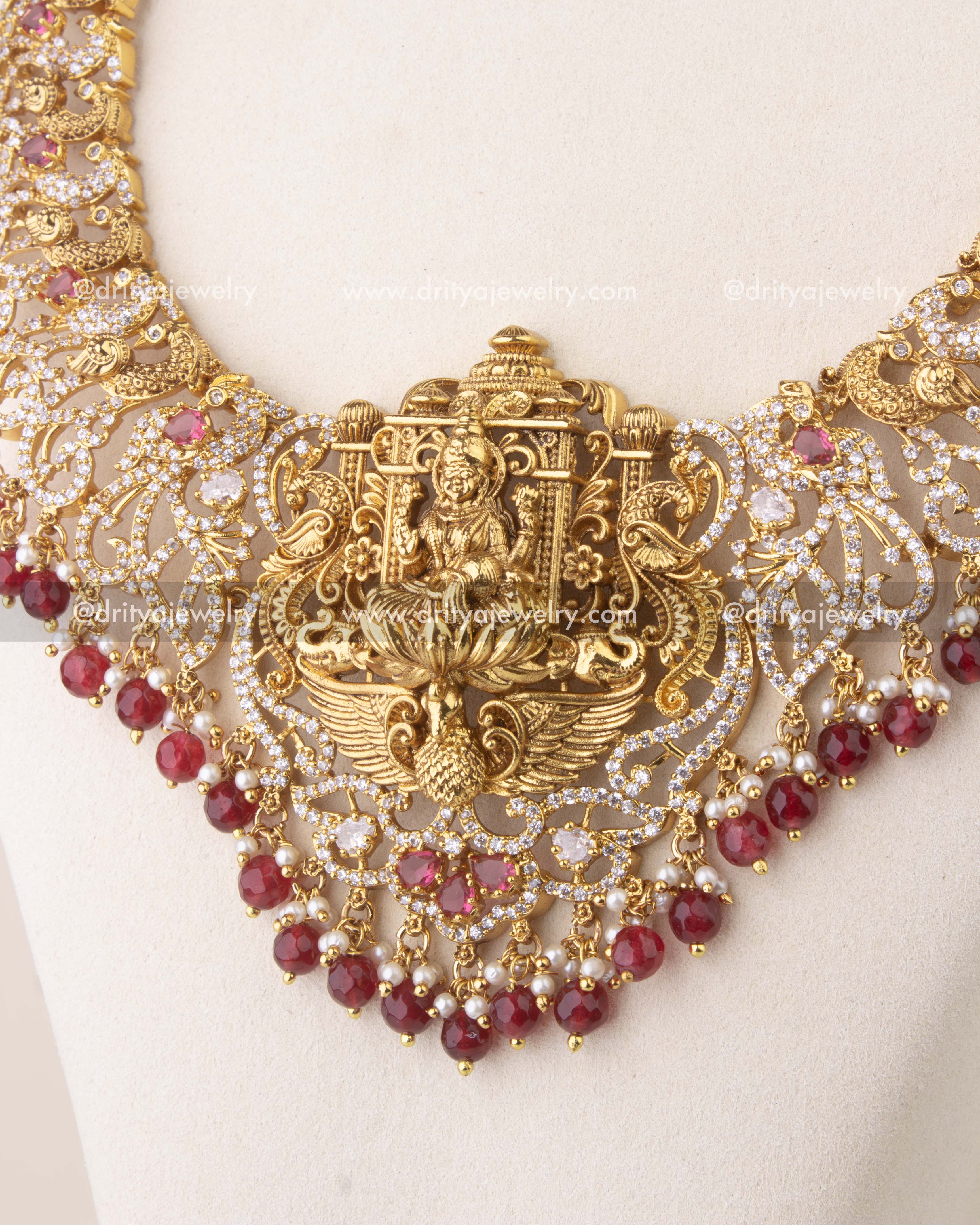 Close-up of Nakshi temple necklace with ruby red stones, peacock motifs, and antique gold finish.
