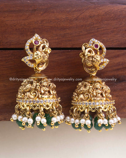 Antique gold peacock jhumkas with nakshi detailing, CZ accents, green beads, and pearl hangings.