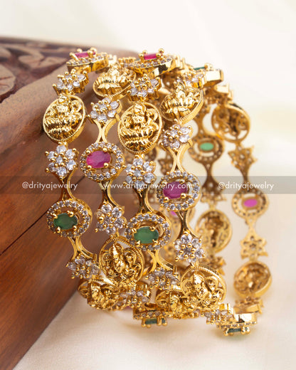 Close-up of premium temple bangles with intricate deity engravings, ruby and green stone mix, and high-shine CZ clusters.