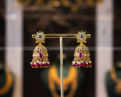 Close-up of Dritya Jewelry's temple-style jhumka earrings with red beads, featuring intricate gold-plated designs and stone embellishments.