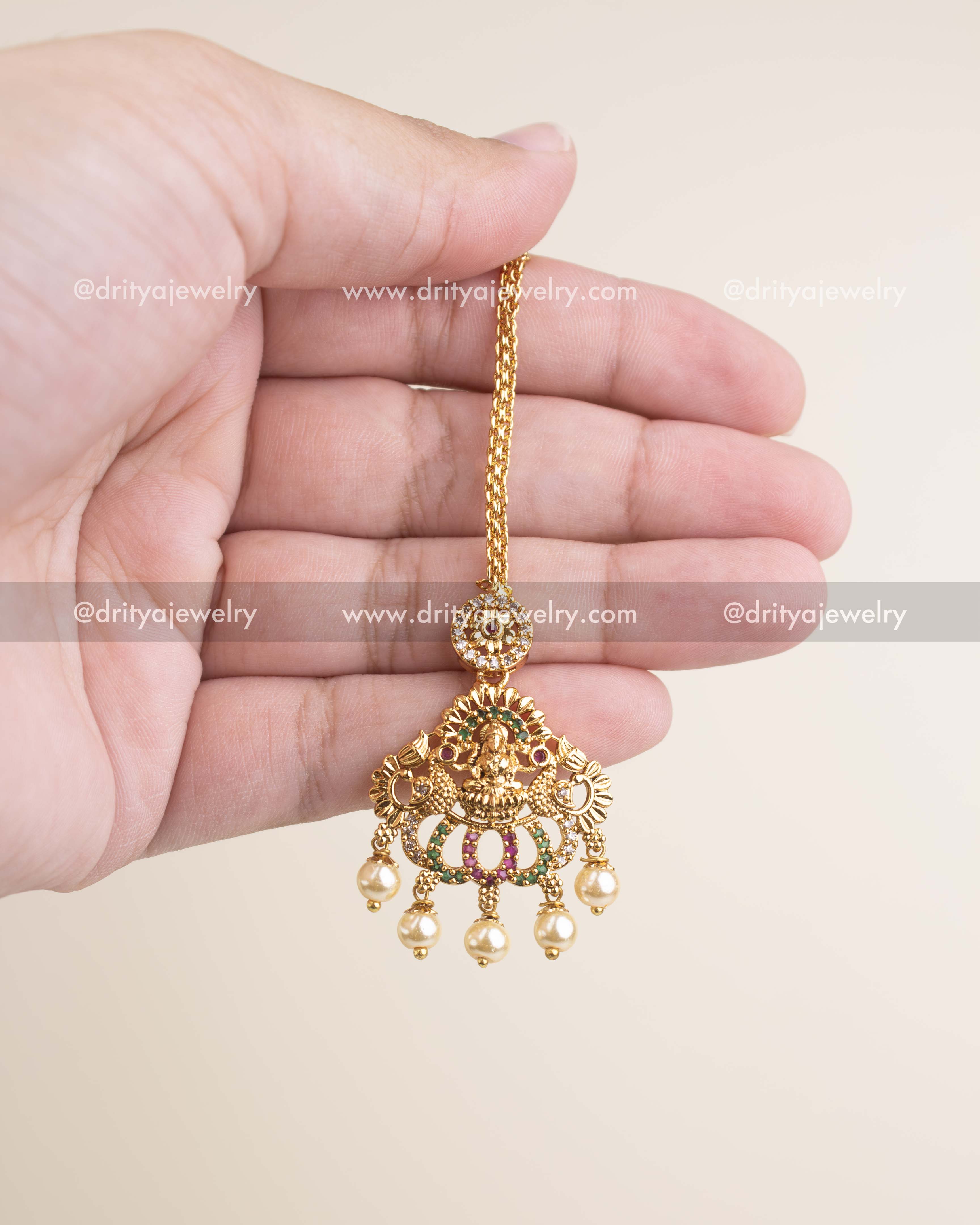 Affordable temple-style maang tikka with goddess motif, pearl droplets and antique gold polish.