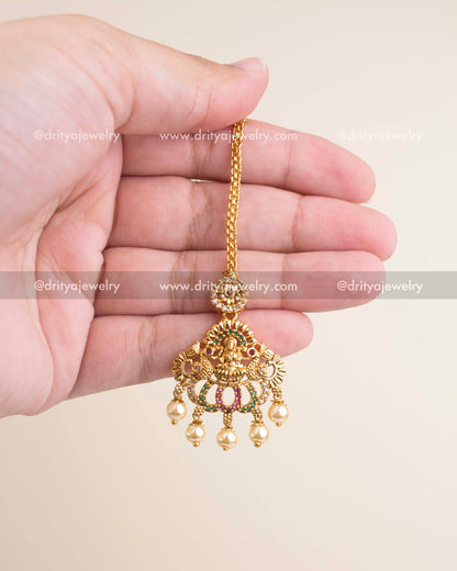 Affordable temple-style maang tikka with goddess motif, pearl droplets and antique gold polish.