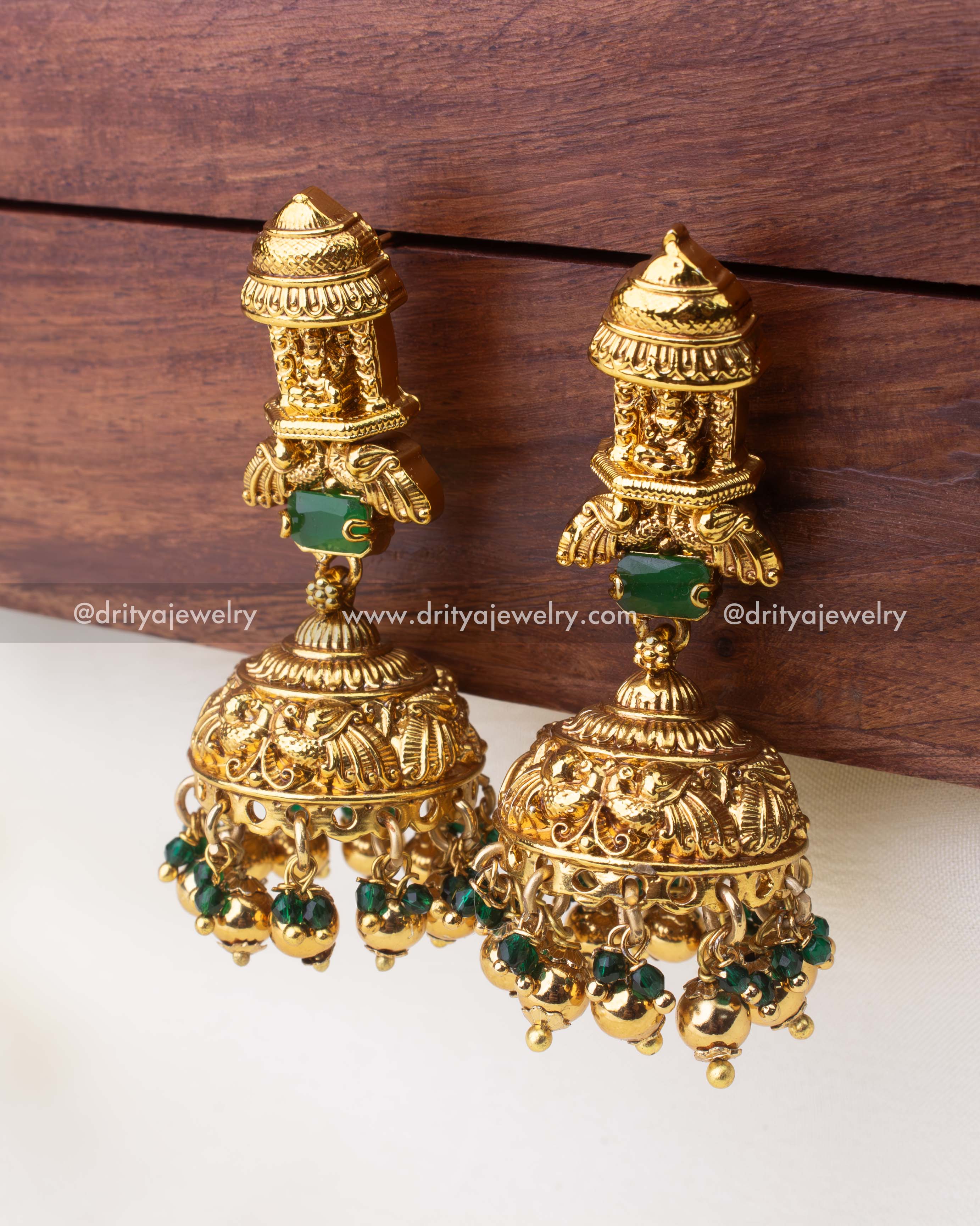 Antique gold temple jhumka earrings featuring Lakshmi motif and green bead drops.