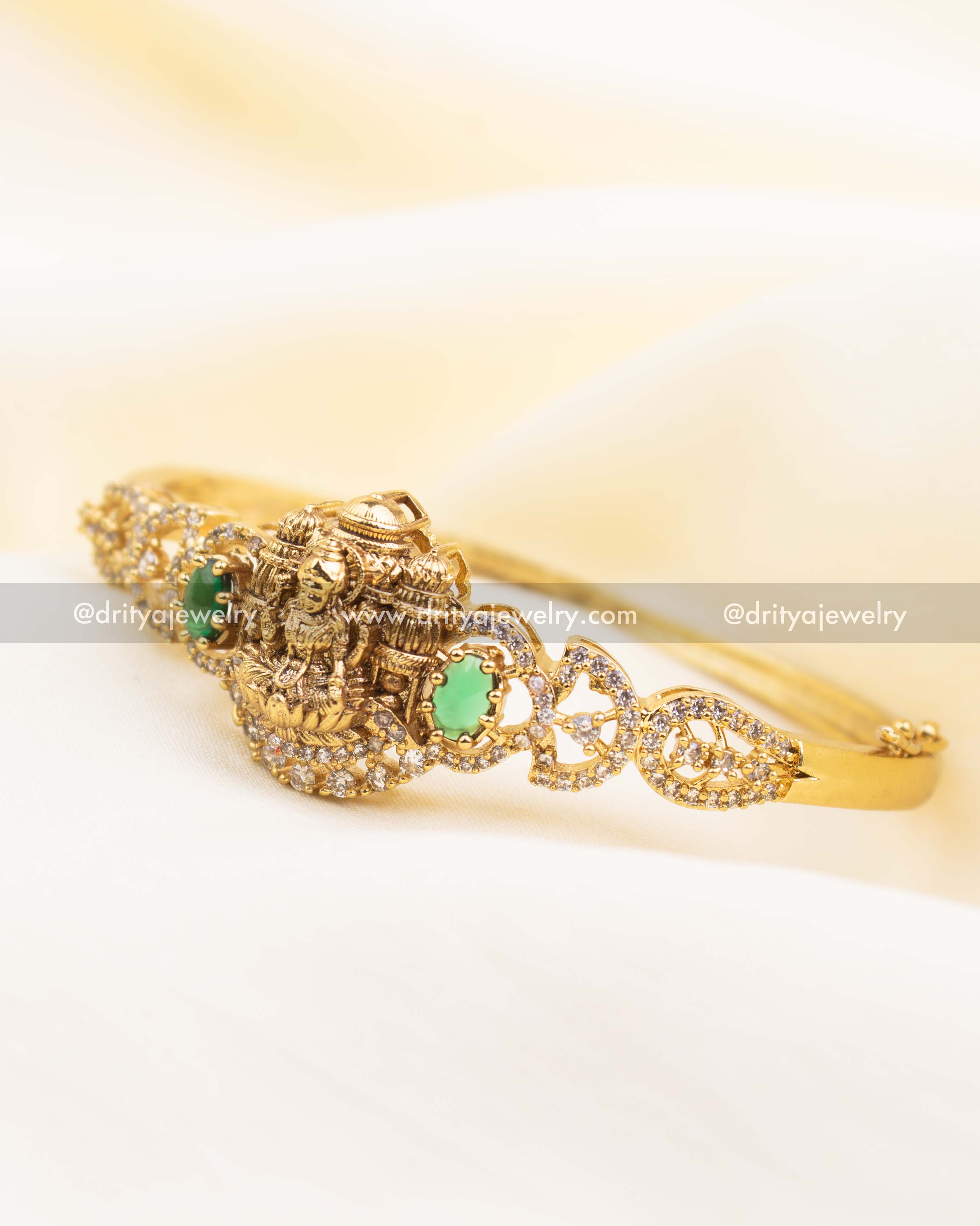 Antique gold adjustable temple kada with Lakshmi motif and emerald green CZ stones surrounded by CZ detailing.