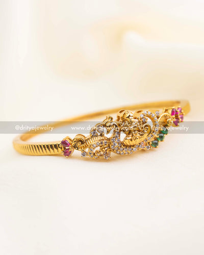 Gold-plated temple kada with ruby and emerald stones in openable design displayed on fabric.