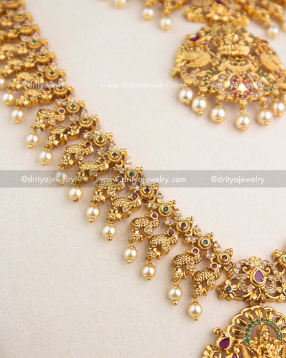 Detailed view of long necklace temple motifs with green and ruby stones and pearls.