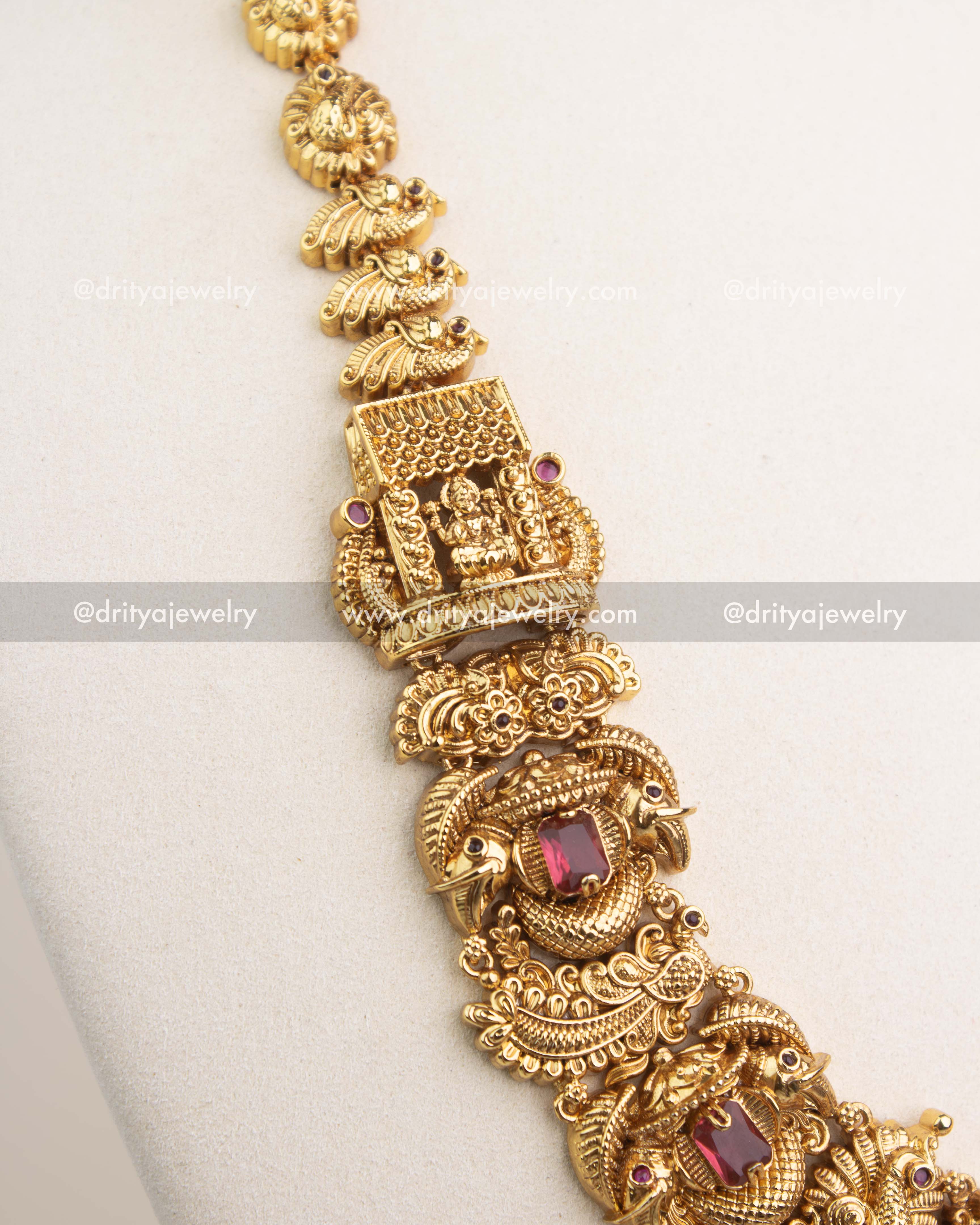 Close-up of gold Nakshi chain with ruby red gemstone settings and traditional motifs.