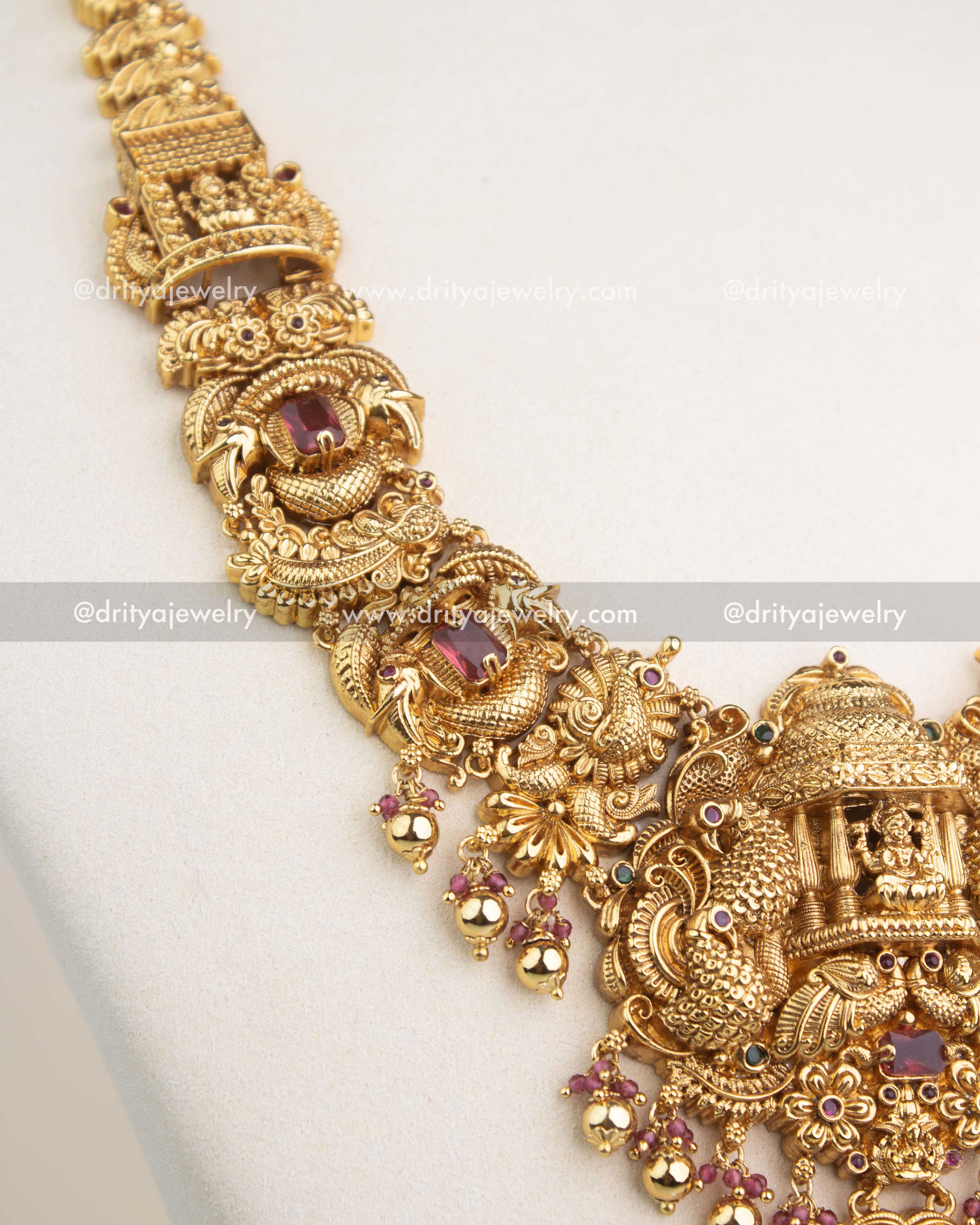 Close-up of gold Nakshi chain with ruby red gemstone settings and traditional motifs.