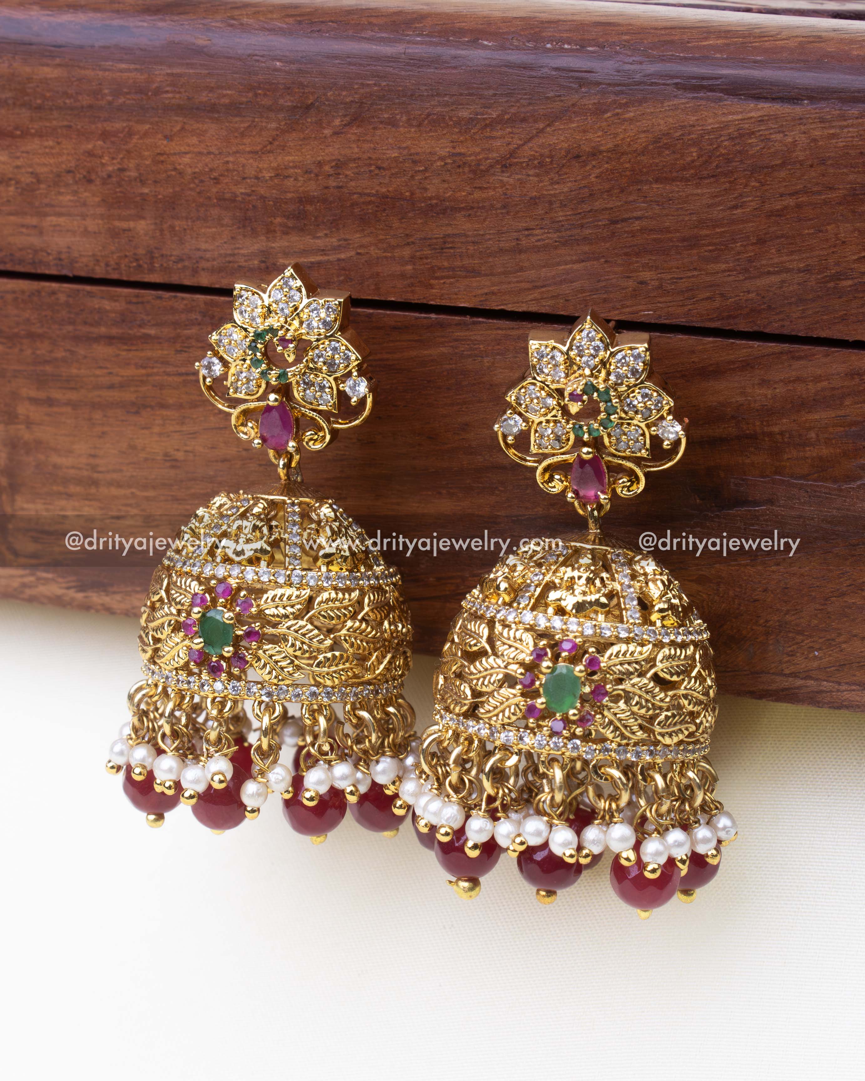 1241-R side angle view of gold-toned temple jhumka earrings with leaf motifs and ruby beads