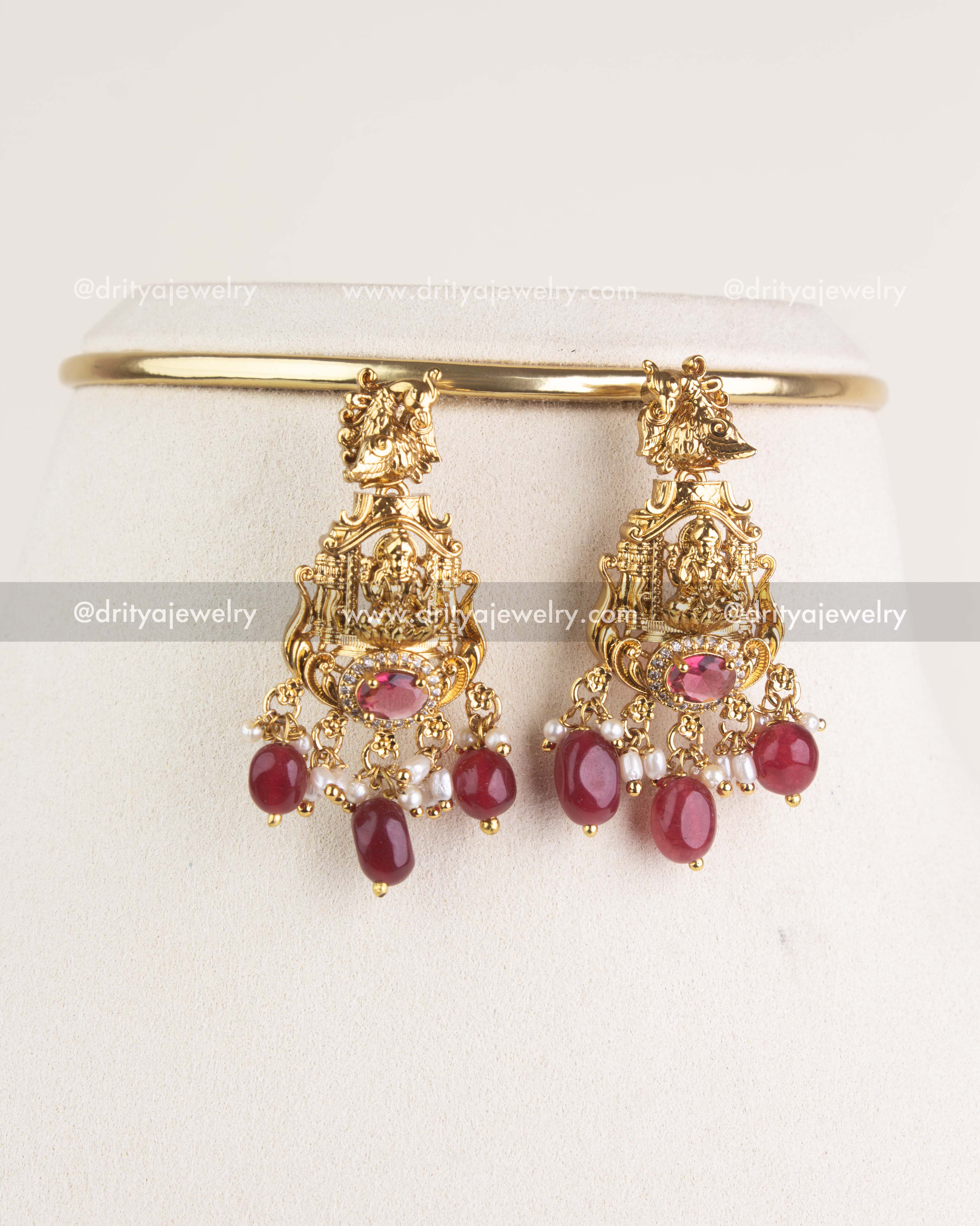 Matching temple earrings with deity motif and ruby bead drops displayed on stand