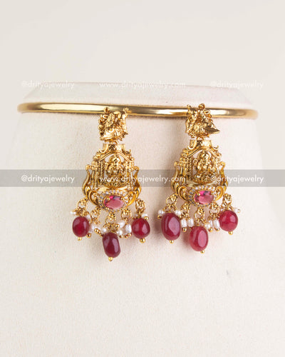 Matching temple earrings with deity motif and ruby bead drops displayed on stand