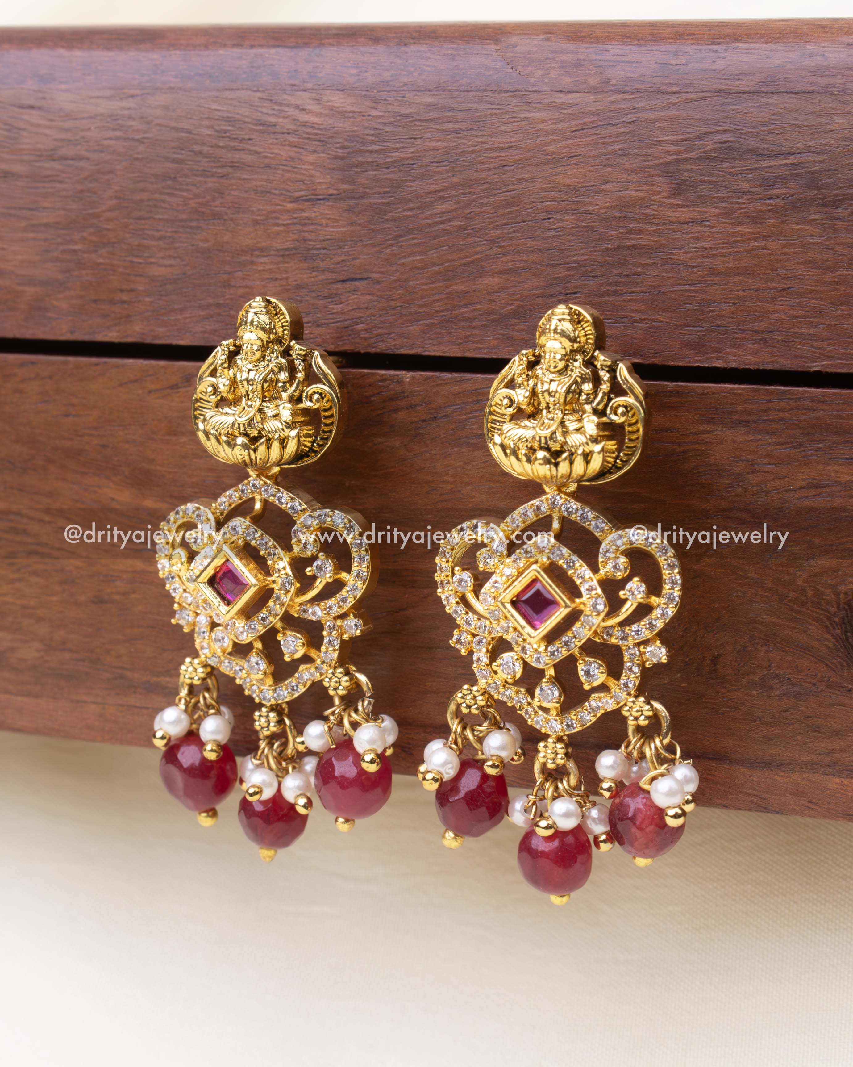 Temple-style imitation earrings with red gemstone drops and intricate deity detail.